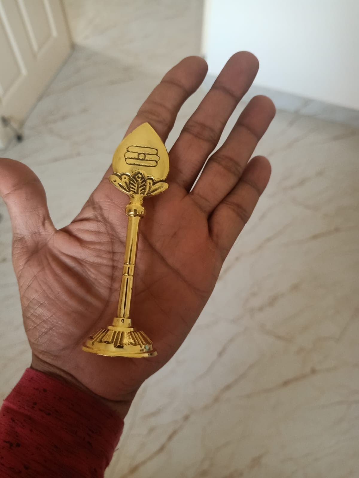 A brass Murugan Vel held in the hand, showing its size